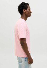 Himmelblaues Baumwoll-T-Shirt mit kurzärmeligem Schnitt, Rundhalsausschnitt und geradem Saum. Das Modell, das es trägt, steht im Profil vor einem neutralen Hintergrund.