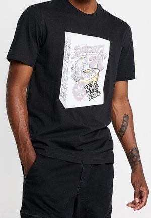 Czarna bawełniana koszulka z nadrukiem z przodu przedstawiającym pudełko płatków śniadaniowych z napisem "Super A" i "Potrójny smak" na białym tle.