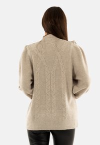 Maglione beige a maglia grossa con collo alto e maniche lunghe. Presenta un design testurizzato sulla parte posteriore e polsini e orlo a costine.