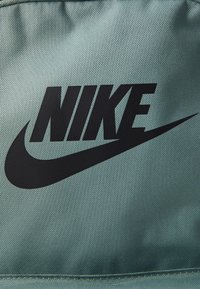 Close-up do logo preto da Nike impresso em um fundo de tecido azul claro texturizado.