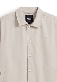 Beige Vans-jack met kraag, drukknoopsluiting, voorzakken en geborduurd Vans-logo op de linkerkant van de borst.