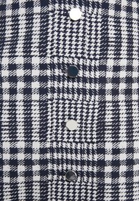 Gros plan d'un tissu pied-de-poule noir et blanc avec quatre boutons ronds brillants alternant noir et blanc, disposés en rangée verticale.