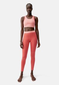 Rózsaszín sportmelltartó és leggings szett rugalmas anyagból. A leggings magas derékkal rendelkezik, sima textúrájú, finom varrási részletekkel.