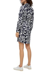 Kleid in Marineblau und Weiß mit gewelltem Muster, Kragen, langen Ärmeln, elastischem Bund, in mittlerer Oberschenkel-Länge, kombiniert mit weißen Sneakers.