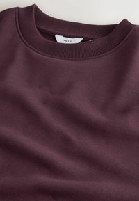 Sweat-shirt col rond violet foncé avec col côtelé et étiquette de marque visible à l’intérieur de l’encolure.