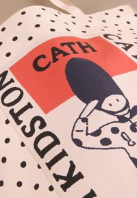 Bavlněná taška s bílým pozadím s černými puntíky, červeným čtvercem a grafickou potiskem postavy s velkým kloboukem a motýlkem.