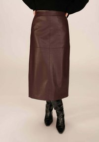 Jupe midi en cuir bordeaux avec une texture lisse, dotée d'une silhouette droite et d'une taille. Accordée avec des bottes noires moulantes jusqu'aux genoux.