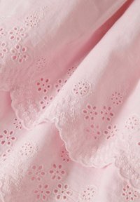 Tissu rose clair doté d'une broderie délicate avec des motifs floraux et des bords festonnés, mettant en valeur la texture et le savoir-faire.