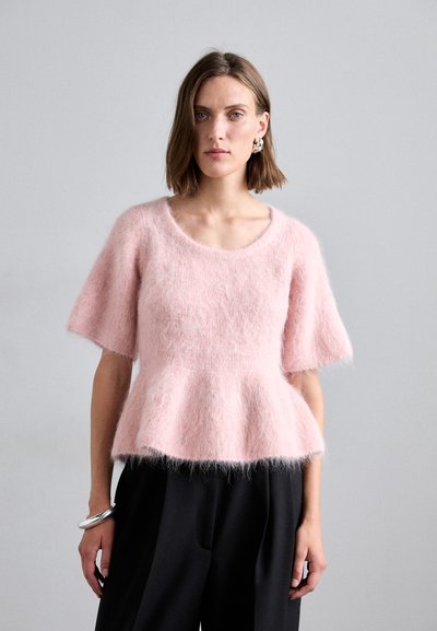 Top knit fluffy rosa chiaro con maniche corte e vita a peplo. Presenta un collo rotondo e una finitura morbida e testurizzata. Abbinato a pantaloni neri.