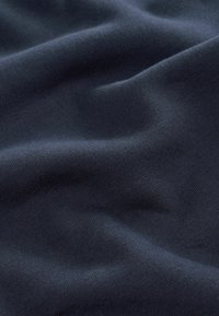 Țesătură închisă, cu o suprafață netedă, ușor texturată, care evidențiază cute și valuri blânde. Culoarea este un albastru navy profund.