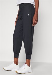 Black jogger pants with a tapered design, elastic cuffs, and side pockets, paired with white sneakers featuring pink accents.