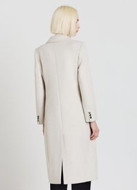 Cappotto in misto lana beige con colletto a rever, maniche lunghe e dettagli a tre bottoni sui polsini, dotato di una spacco centrale sul retro per maggiore comodità.