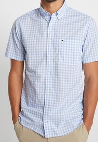 Camicia a maniche corte con bottoni, in un motivo a scacchi blu chiaro e bianco, con taschino sul petto e logo accentuato sul lato sinistro.