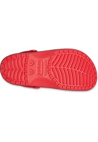 Semelle de sandalettes Crocs rouges avec un motif de bande de roulement texturé, featuring des rainures profondes et le logo de la marque embossé au centre. Design léger et flexible.