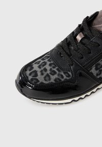 Czarne sneakersy z materiałem w panterkę, błyszczący, lakierowany czubek, czarne sznurówki, detal w postaci zamka oraz biała i czarna żebrowana podeszwa.