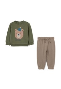 Sudadera verde oliva con un gráfico de un oso y texto, combinada con pantalones jogger beige. Ambos son de materiales suaves y elásticos con dobladillos acampanados.