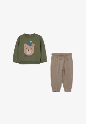 Olijfgroene sweatshirt met een berenafbeelding en tekst, gecombineerd met beige joggerbroeken. Beide zijn gemaakt van zachte, rekbare materialen met boordjes aan de onderkant.