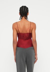 Bordowa satynowa koszulka na ramiączkach z cienkimi ramiączkami, dopasowany krój, gładka faktura i warstwowy dół, w zestawieniu z szarymi spodniami od garnituru.