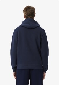 Mörkblå hoodie av mjukt tyg, med en stor huva, ribbade ärmslut och rak nederkant. Inga synliga logotyper eller mönster.