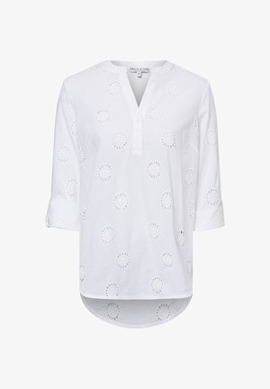 Weiße Bluse mit langen Ärmeln, rundem Ausschnitt, Knopfleiste und kreisförmigen Ösenmustern, die gleichmäßig im Stoff verteilt sind.