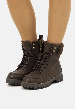 Braune Schnürstiefeletten mit synthetischem Obermaterial, strukturiertem Fleecebund, gepolsterter Oberkante und robuster Gummisohle. Mit metallischen Akzenten und Reißverschluss.