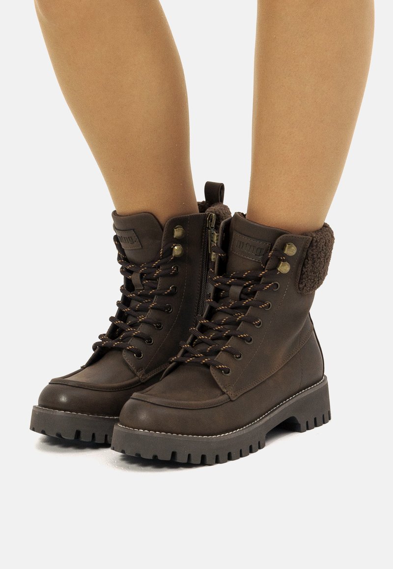 Botas de tobillo con cordones en color marrón, con parte superior sintética, puño de felpa texturizada, cuello acolchado y suela de goma resistente. Presenta detalles metálicos y cremallera.