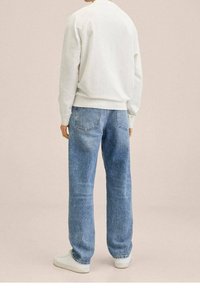 Biała bawełniana bluza z prążkowanymi mankietami, zestawiona z jasnoniebieskimi dżinsami o luźnym kroju i dwoma tylnymi kieszeniami. Całość dopełniają białe trampki.