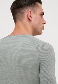 T-shirt de mangas longas cinza claro com um padrão texturizado em nervuras e mangas raglan, apresentando um decote redondo e ombros sem costura.