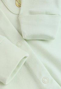 Body bébé vert pâle doux avec manches repliées et boutons-pression à l'avant pour un habillage et un change faciles.