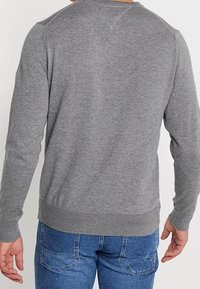 Sudadera gris de manga larga con cuello redondo, puños y dobladillo acanalados. Presenta una textura suave y costuras en los hombros con un ligero detalle.