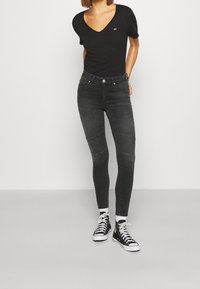 Camiseta negra de cuello en V combinada con vaqueros ajustados negros con paneles y costuras blancas, completados con zapatillas altas negras.