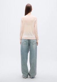 Μπεζ μακρυμάνικη μπλούζα με λεπτή υφή, συνδυασμένη με ψηλόμεσα, φαρδιά ανοιχτό μπλε τζιν με κλασικές πίσω τσέπες.