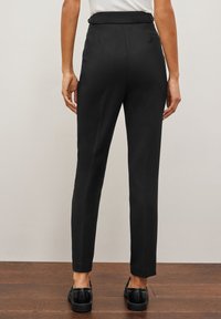 Zwarte, op maat gemaakte broeken met een recht model, met een gladde textuur, een middelhoge taille en minimale details. Draag met zwarte schoenen.