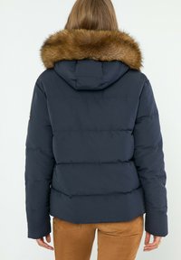Granatowa kurtka puchowa z kapturem i sztucznym futrem, z pikowanym wzorem i lekko skróconą długością. Brak widocznego zapięcia z przodu.