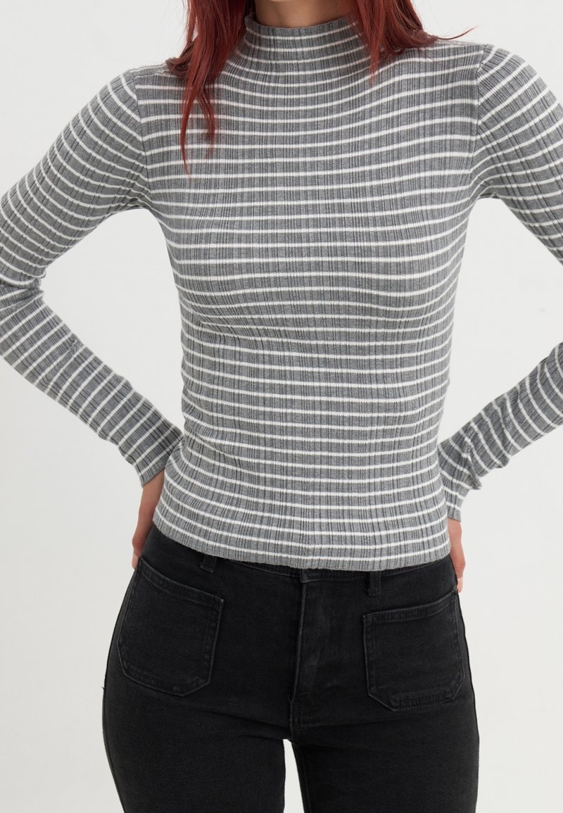 Paskowany longsleeve z wysokim kołnierzem, wykonany z szarego prążkowanego materiału z cienkimi białymi paskami. W zestawie z czarnymi dżinsami.