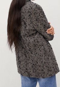 Kurtka w wzór houndstooth w czerni i kremie, charakteryzująca się dopasowanym krojem o lekko teksturowanej powierzchni. Długie rękawy i średnia długość.