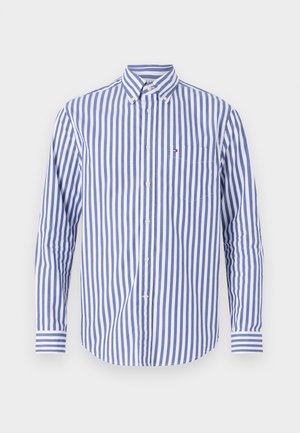 Camicia a righe blu e bianca. Presenta maniche lunghe, un colletto e una tasca sul petto con un piccolo dettaglio del logo.