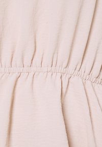 Tissu rose avec une apparence douce et texturée. La taille élastique froncée crée une forme fluide, adaptée à une tenue décontractée.