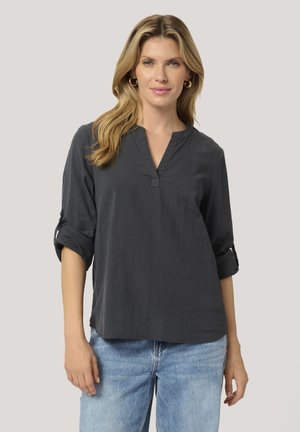 Dark gray, textured blouse with a V-neckline and rolled sleeves. Worn with light blue jeans, featuring a relaxed fit.