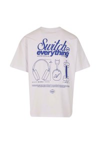 Hvid t-shirt med blå grafisk tekst "Sluk alt" samt detaljerede illustrationer af hovedtelefoner og andre genstande nedenfor.