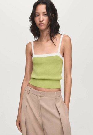 Green knitted crop top with white straps, featuring a square neckline and a fitted hem. Paired with beige high-waisted trousers.
