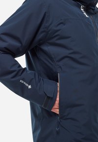 Navy blue, waterproof jacket made of smooth fabric, featuring a zippered pocket, velcro cuffs, and a logo on the sleeve.