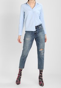 Ljusblå skjorta med uppknäppta knappar, slitna blåjeans och blommiga mönstrade strumpor med högklackade skor. Framträdande färger inkluderar blått, svart och rosa.