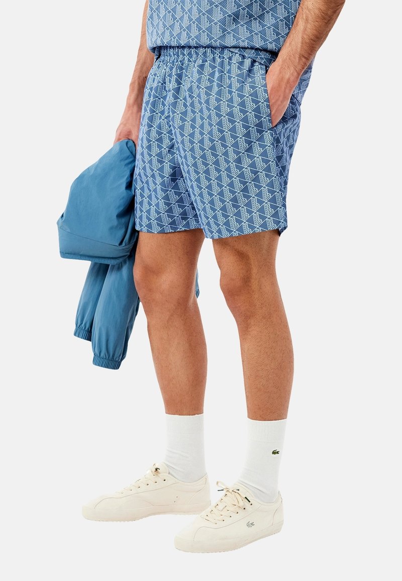 Pantalones cortos azul con estampado y cintura elástica, combinados con una chaqueta ligera a juego, calcetines blancos y zapatillas color crema.