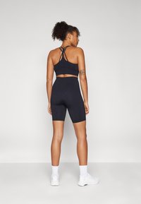 Crna sportska bralette s preklopnim leđnim trakama u kombinaciji s crnim hlačama viskog struka. Glatka tekstura tkanine, minimalistički dizajn, bez uzoraka.