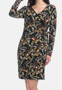 Robe noire portefeuille avec manches longues et motif floral en orange, blanc et vert, présentant une silhouette ajustée et des détails froncés à la taille.