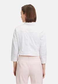 Weiße, kurz geschnittene Jeansjacke mit langen Ärmeln, Knopfkragen und einer Nahtdetail an der hinteren Passe, kombiniert mit hellrosa Hosen.