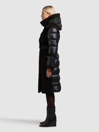 Fekete steppelt pufi kabát puha tapintású oldalsó résszel, magas gallérral és övvel. Fényes anyagból készült, steppelt mintázattal. Elegáns fekete csizmával viselve.