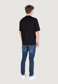 T-shirt nera a maniche corte con collo rotondo, abbinata a jeans slim-fit blu. Il modello indossa sneaker bianche e ha un'acconciatura riccia e texturizzata.