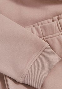 Nærbillede af blød, lys pink stof, der viser en ribbet manchet og talje fra et sweatshirt- og joggersæt, med fokus på tekstur og farve.